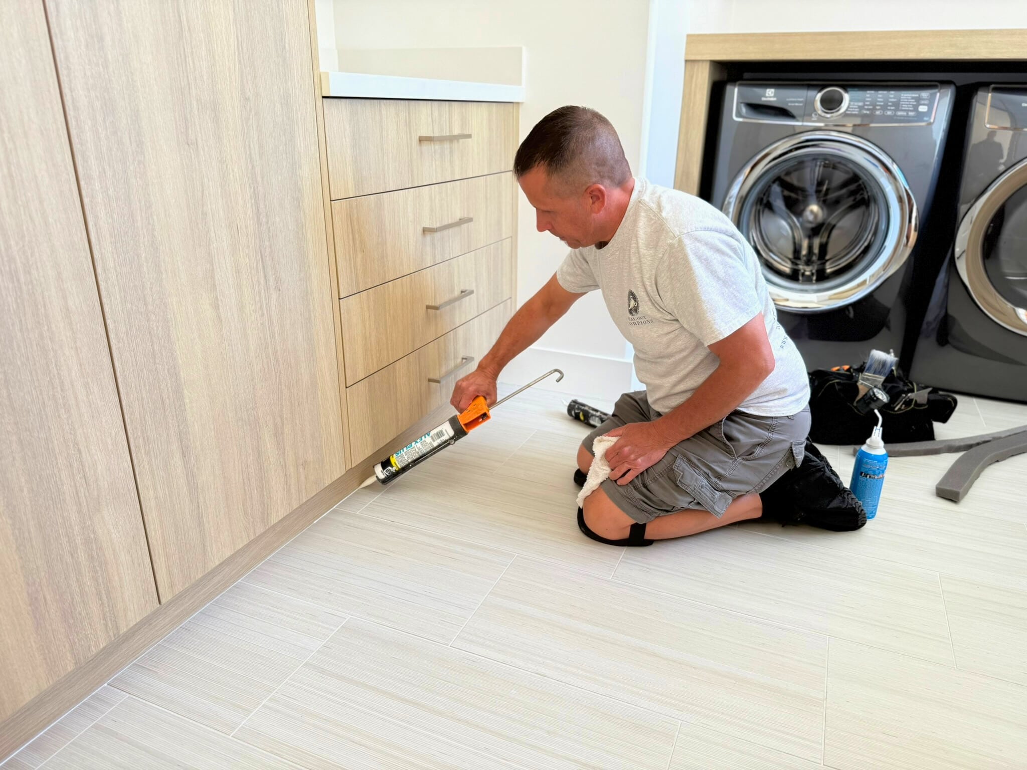 Jeff Sealing the base of a cabinet in a modern laundry room using a caulking gun