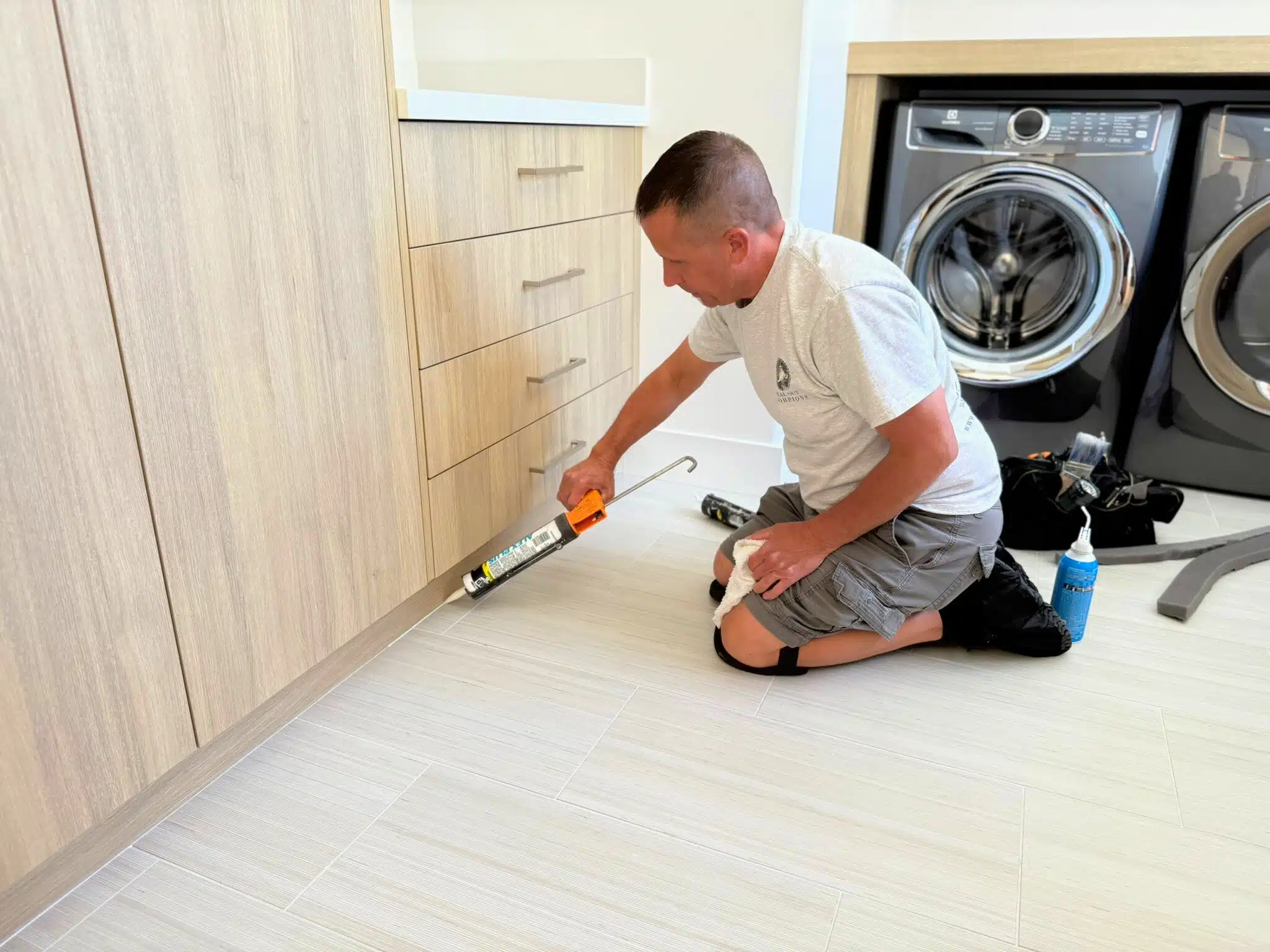 Jeff Sealing the base of a cabinet in a modern laundry room using a caulking gun