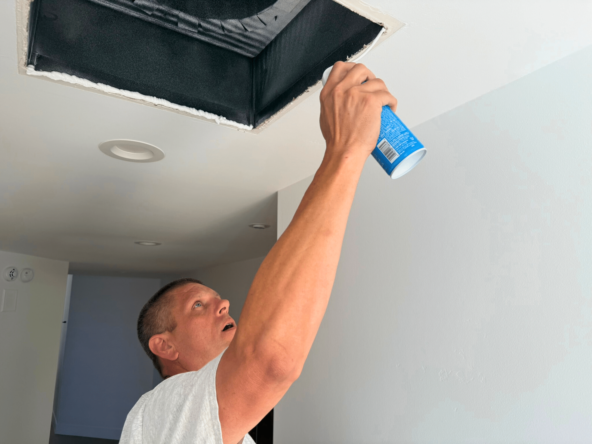 Mike With Blue Can applying spray foam for Building Performance Sealing around a ceiling vent