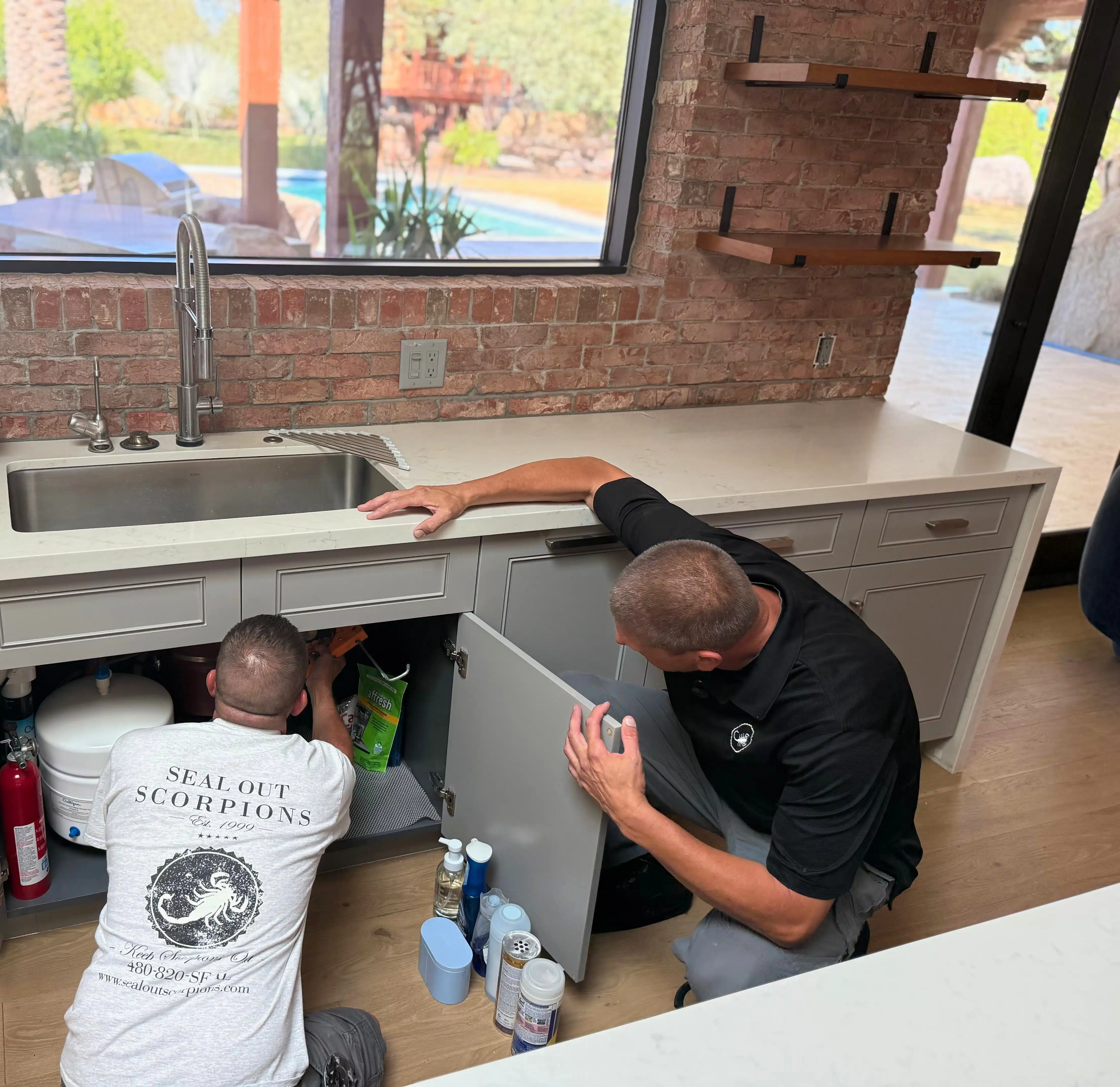 Technicians applying an under sink seal as part of Building Performance Sealing™ to control airflow and prevent pest entry