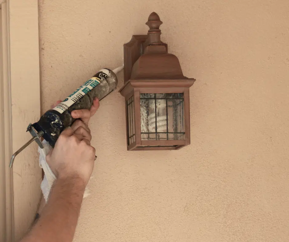 Technician applying caulk to a light fixture, highlighting sealing challenges in desert environments